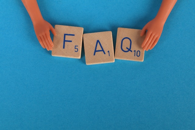 A close-up shot of Scrabble tiles spelling FAQ on a blue surface.