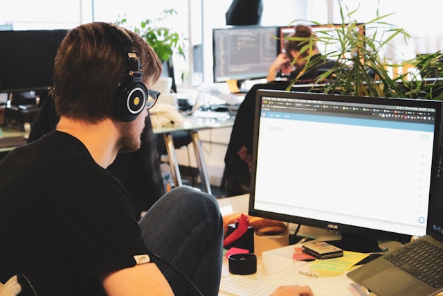 A person with black headphones uses a computer in an office.