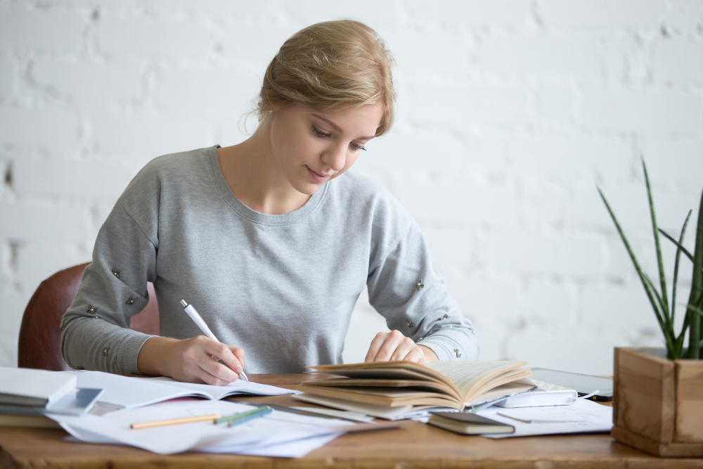 A person copies text from a book to a white sheet of paper.