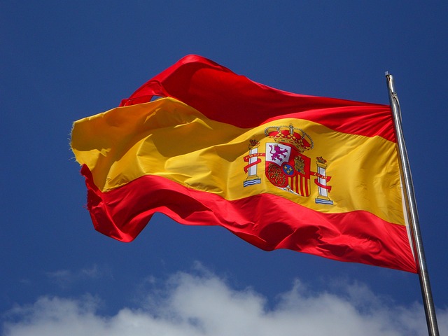 A Spanish flag on a pole fluttering in the wind in the daytime.
