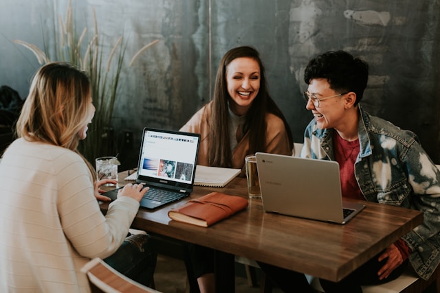 Three people sit at a brown wooden table and laugh.