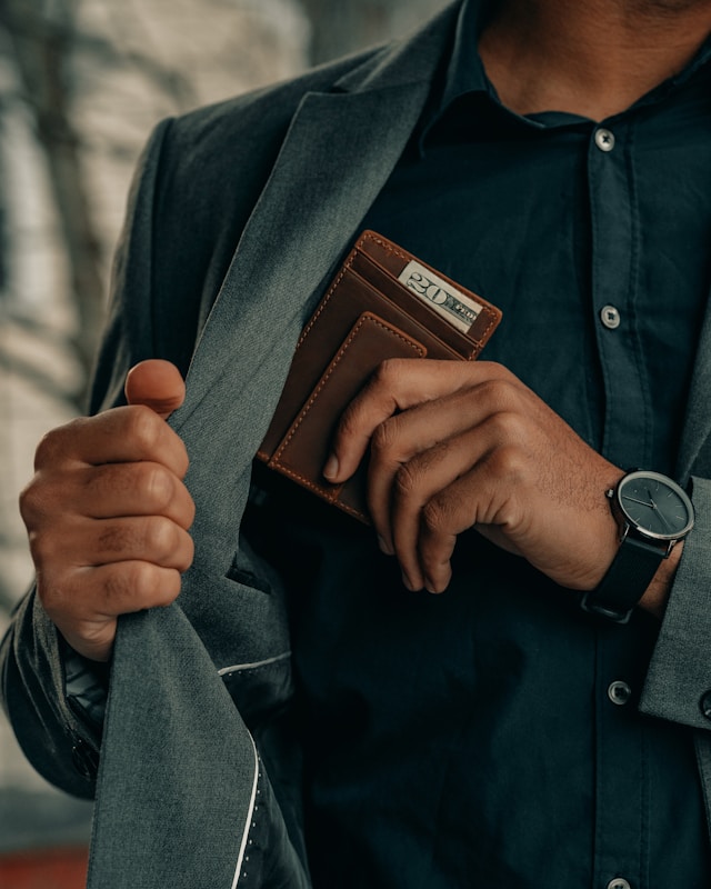 A person with a green jacket holds a wallet with a 20 dollar bill.