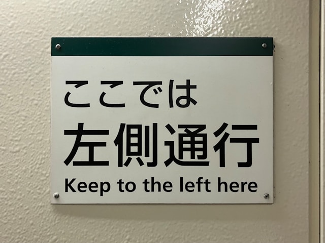 A close-up of a sign on a white wall in three languages.
