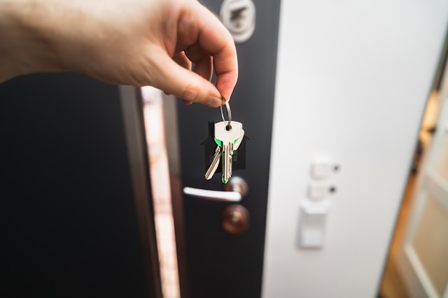 A person holds several keys with a black keychain in front of a door.