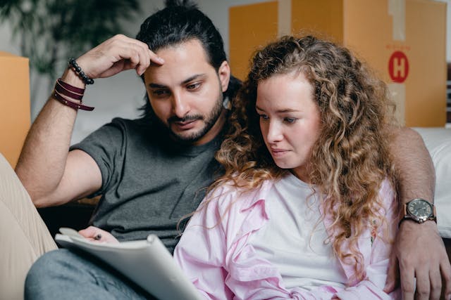 A man with a black shirt and a woman with a pink shirt look at a notebook.
