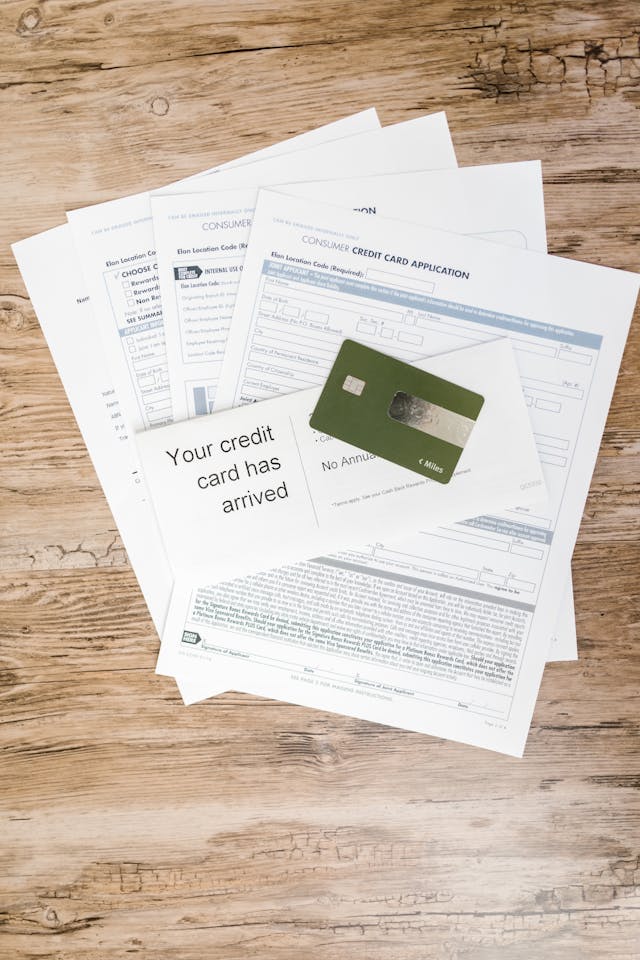 A green-colored credit card in front of several sheets of paper on a brown wooden table.