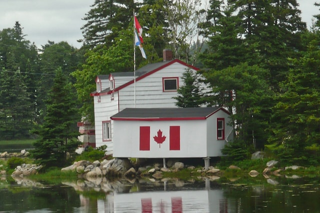 A close-up of a house near a water body with a Canadian flag on its wall.