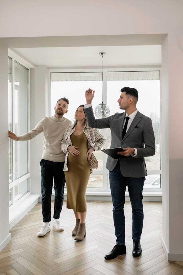 A real estate agent in a gray suit shows a house to a couple.