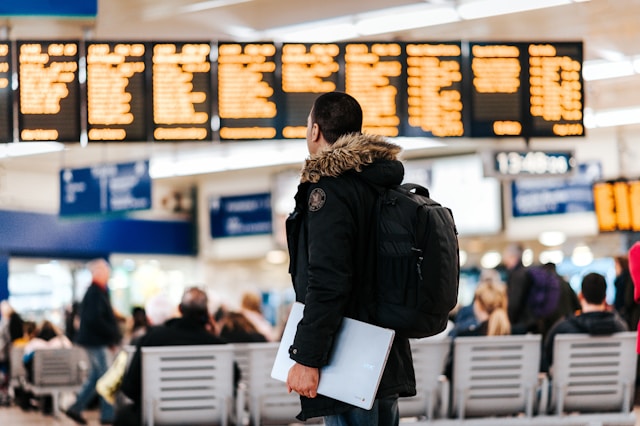 A person with a black jacket looks at a digital board with multiple flight schedules.